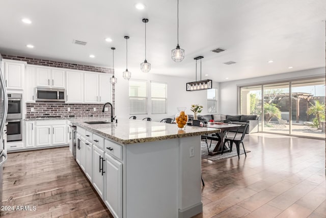 kitchen with white cabinetry, light stone countertops, sink, an island with sink, and appliances with stainless steel finishes