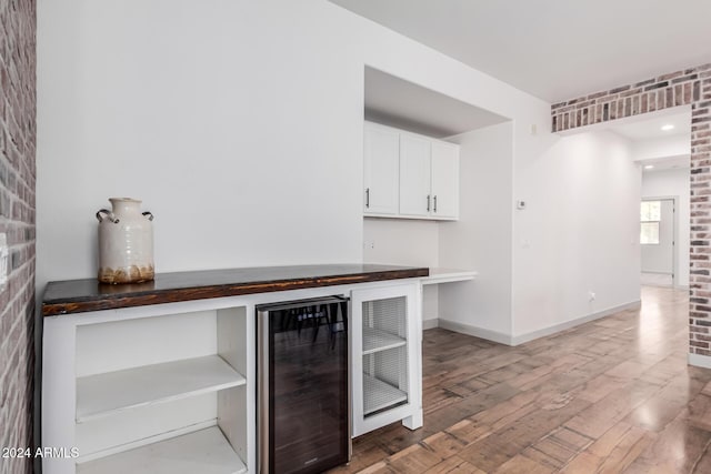 bar with wine cooler, hardwood / wood-style floors, white cabinets, and brick wall