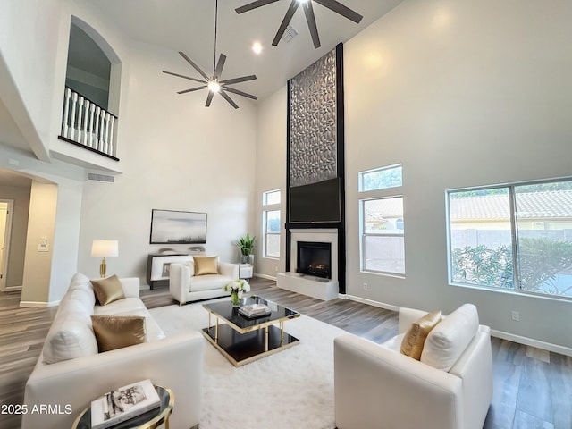 living room featuring ceiling fan, a large fireplace, high vaulted ceiling, and hardwood / wood-style floors