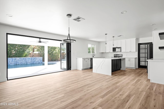 kitchen with visible vents, hanging light fixtures, open floor plan, white cabinets, and a kitchen island