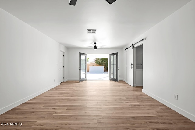 unfurnished room featuring a barn door, visible vents, baseboards, a ceiling fan, and light wood-type flooring