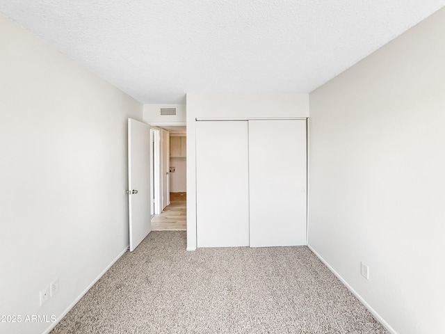 unfurnished bedroom featuring visible vents, a textured ceiling, a closet, carpet, and baseboards