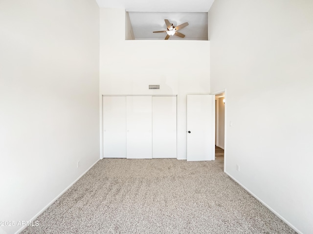 unfurnished bedroom featuring visible vents, a high ceiling, a closet, and carpet flooring