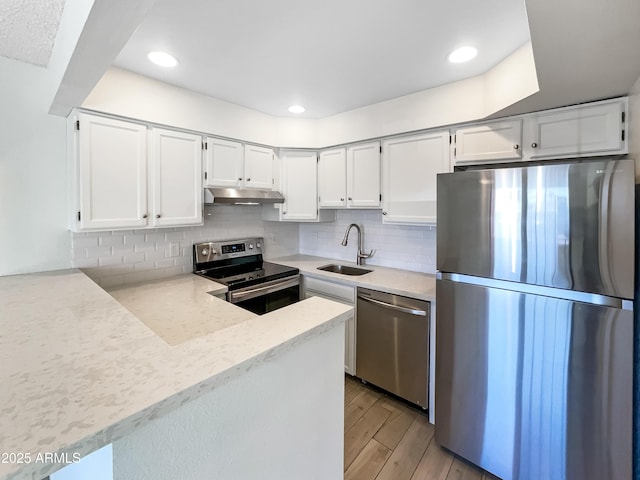 kitchen featuring a sink, white cabinets, under cabinet range hood, appliances with stainless steel finishes, and backsplash