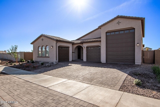 mediterranean / spanish-style house with an attached garage, fence, decorative driveway, and stucco siding