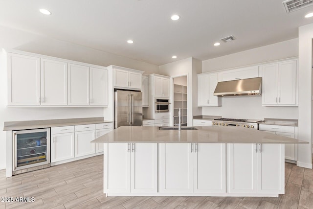 kitchen with beverage cooler, stainless steel appliances, under cabinet range hood, white cabinetry, and a sink