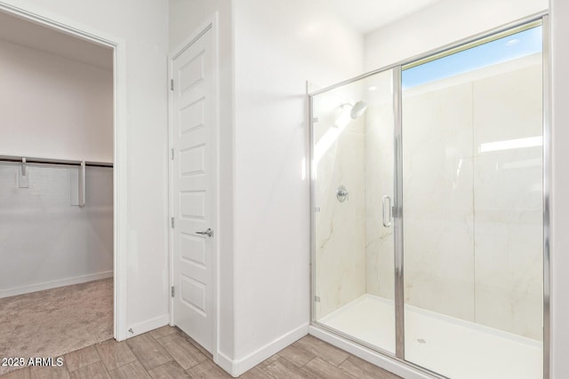 bathroom featuring a shower stall, wood tiled floor, baseboards, and a walk in closet