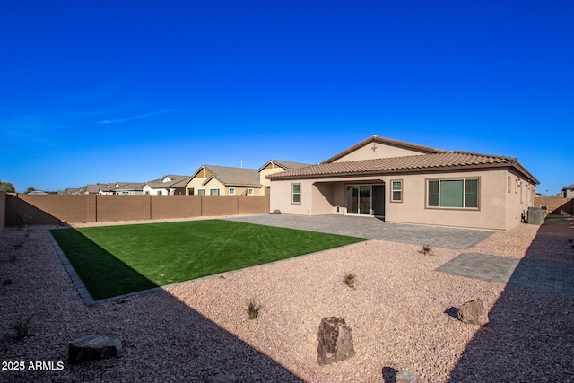 back of house featuring a lawn, a fenced backyard, a tiled roof, a patio area, and stucco siding