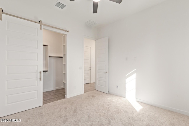 unfurnished bedroom featuring carpet floors, visible vents, a spacious closet, a barn door, and baseboards