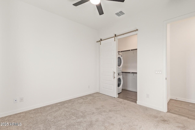 unfurnished bedroom featuring a walk in closet, stacked washer and clothes dryer, visible vents, a barn door, and carpet flooring