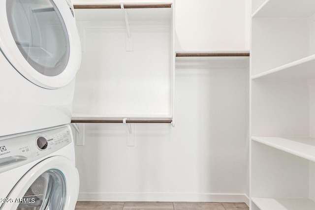 laundry area with laundry area, stacked washer / dryer, light wood-type flooring, and baseboards