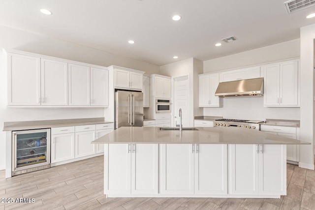 kitchen featuring wine cooler, stainless steel appliances, white cabinetry, a sink, and under cabinet range hood