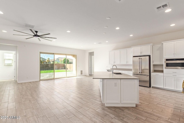 kitchen featuring visible vents, appliances with stainless steel finishes, open floor plan, white cabinetry, and a sink