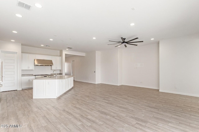 kitchen with under cabinet range hood, visible vents, light wood-style floors, open floor plan, and an island with sink