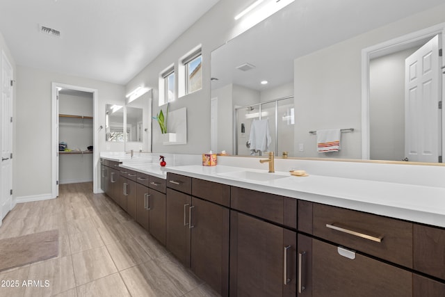 bathroom featuring double vanity, visible vents, a stall shower, a sink, and baseboards