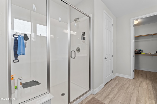 bathroom with a shower stall, a spacious closet, and baseboards