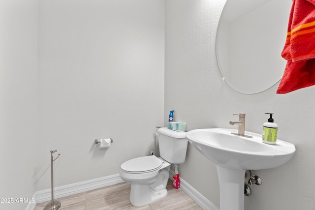 half bathroom featuring wood finished floors, toilet, and baseboards