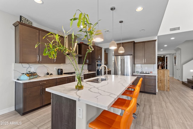 kitchen with pendant lighting, stainless steel appliances, visible vents, a sink, and wall chimney exhaust hood