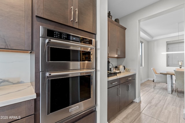 kitchen with baseboards, double oven, dark brown cabinetry, and light stone countertops