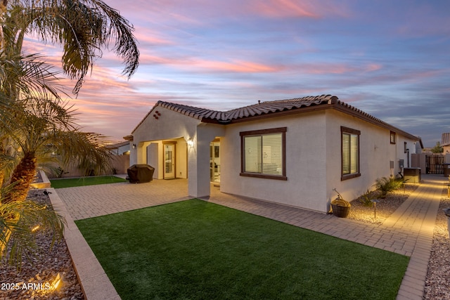 22837 E Silver Creek Ln, Queen Creek, AZ 85142 - back of house at dusk featuring a tiled roof, decorative driveway, a yard, a patio area, and stucco siding