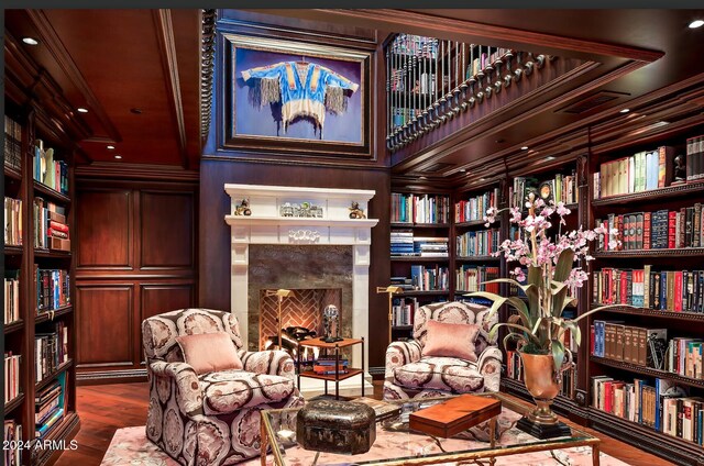 living area with built in shelves, wood-type flooring, crown molding, and a high end fireplace