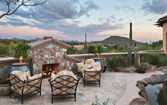 patio terrace at dusk with an outdoor stone fireplace and a mountain view