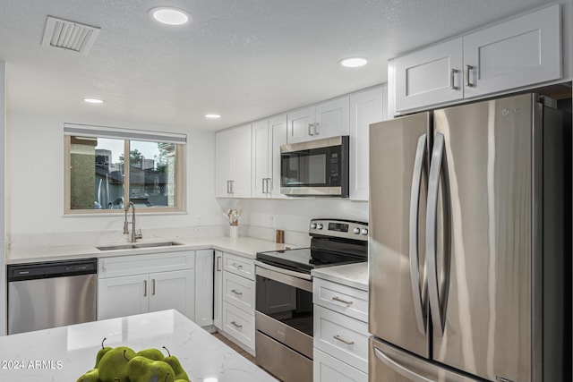 kitchen with stainless steel appliances, sink, light stone countertops, white cabinets, and a textured ceiling