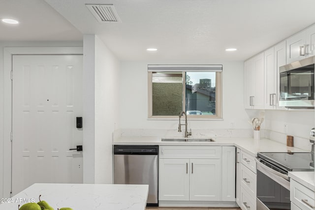 kitchen with appliances with stainless steel finishes, white cabinets, sink, and light stone counters