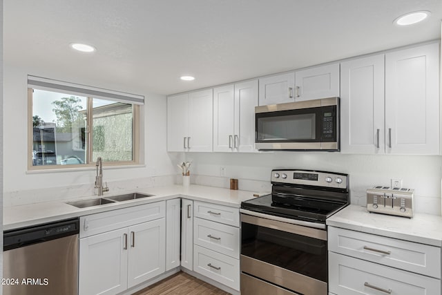 kitchen with light hardwood / wood-style flooring, stainless steel appliances, sink, white cabinets, and light stone counters