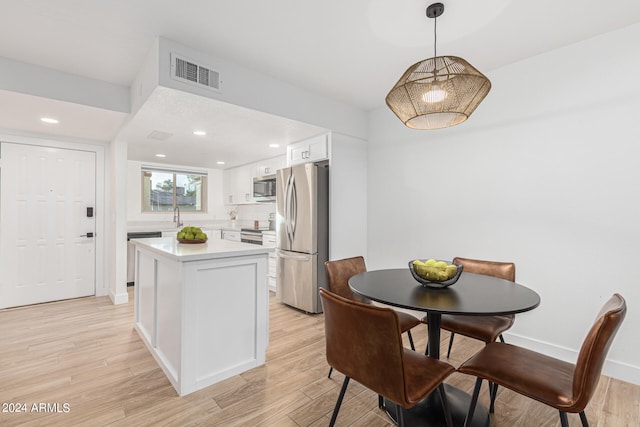 kitchen with light hardwood / wood-style flooring, hanging light fixtures, stainless steel appliances, sink, and white cabinetry