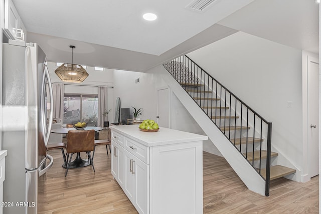 kitchen featuring light hardwood / wood-style flooring, hanging light fixtures, white cabinets, and stainless steel refrigerator