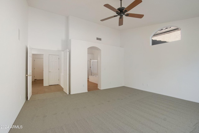 spare room with ceiling fan, a towering ceiling, and light carpet