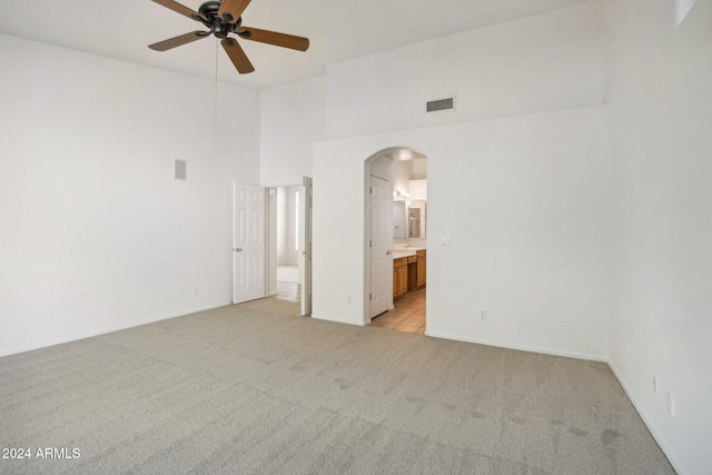 spare room with ceiling fan, a towering ceiling, and light carpet