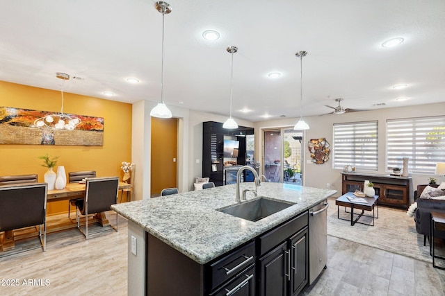 kitchen featuring an island with sink, decorative light fixtures, light hardwood / wood-style flooring, light stone counters, and sink