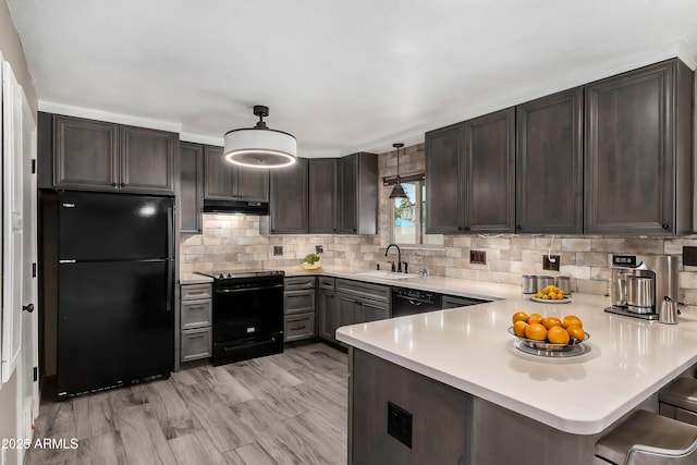 kitchen with pendant lighting, sink, black appliances, a kitchen bar, and kitchen peninsula