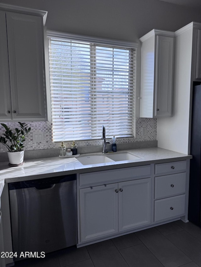 kitchen with backsplash, sink, stainless steel dishwasher, dark tile patterned floors, and white cabinetry