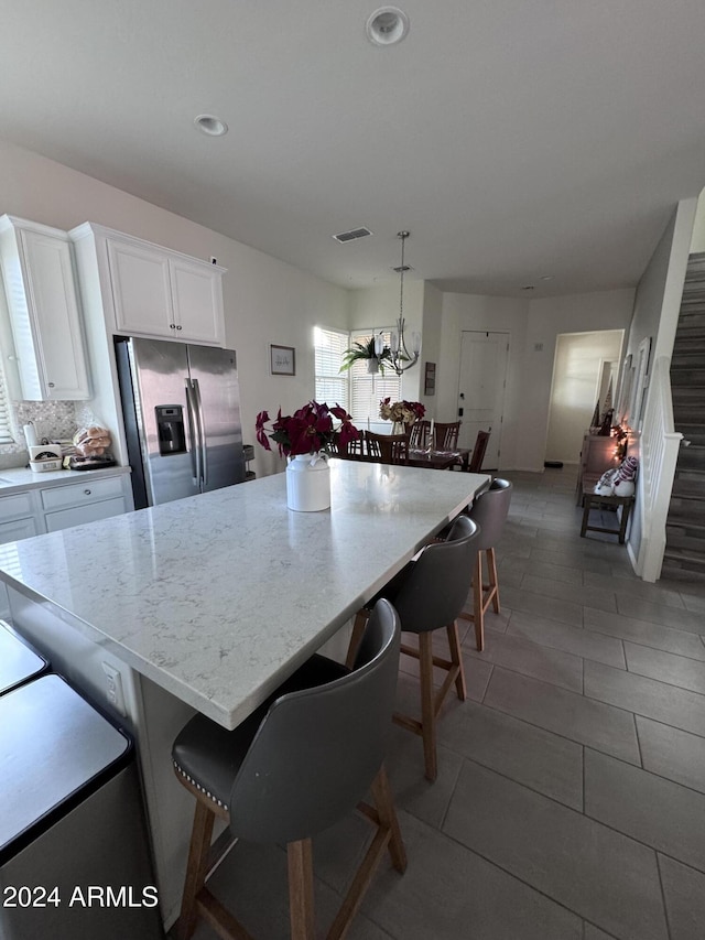 kitchen featuring a kitchen breakfast bar, light stone counters, decorative light fixtures, white cabinets, and stainless steel fridge with ice dispenser