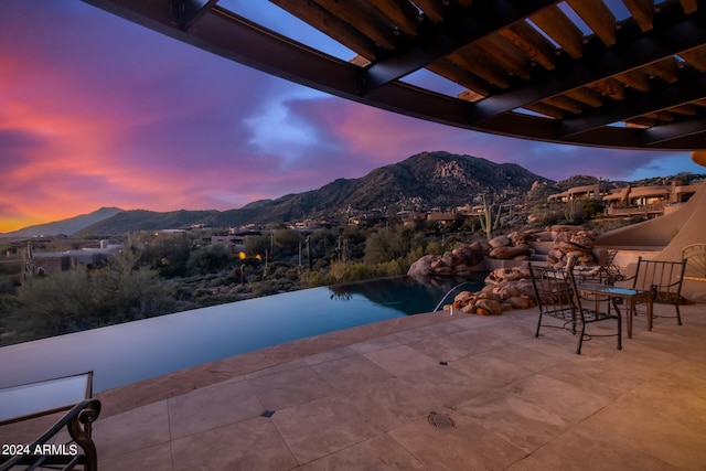 pool at dusk featuring a mountain view and a patio area