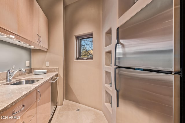 kitchen with appliances with stainless steel finishes, light stone counters, light brown cabinets, and sink