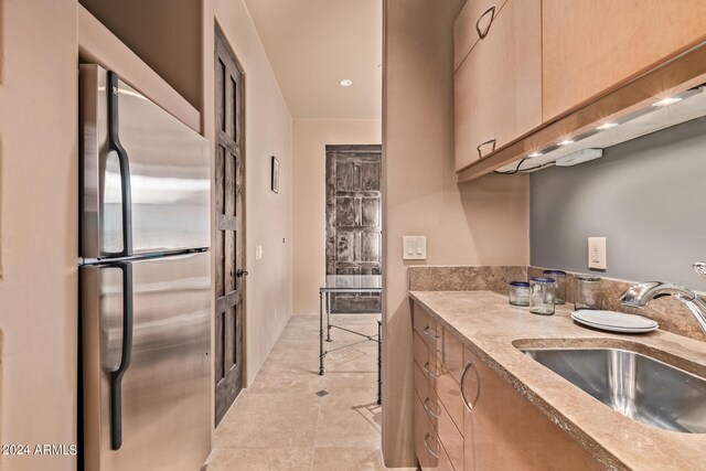 kitchen featuring light brown cabinetry, stainless steel refrigerator, sink, and light tile floors