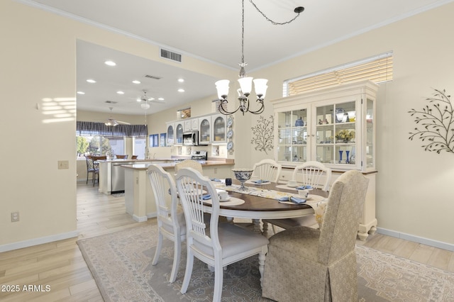 dining area with crown molding, ceiling fan with notable chandelier, and light hardwood / wood-style floors