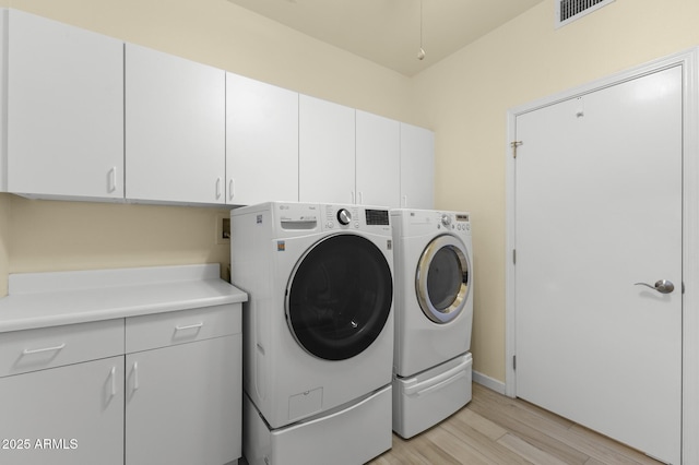 laundry room featuring cabinets, washer and dryer, and light hardwood / wood-style flooring