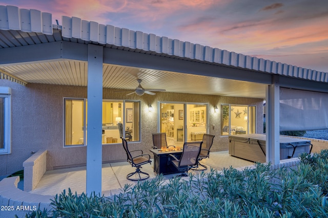 patio terrace at dusk with a fire pit, a hot tub, and ceiling fan