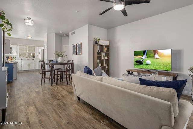 living room with a textured ceiling, dark wood-type flooring, and ceiling fan