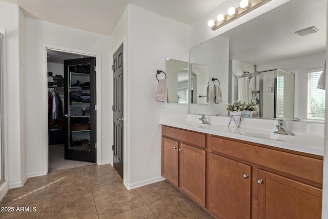 bathroom with a walk in closet, double vanity, visible vents, a stall shower, and a sink