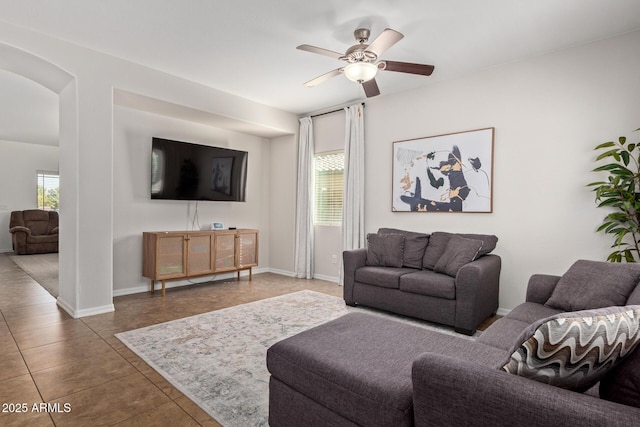 tiled living area featuring arched walkways, ceiling fan, and baseboards