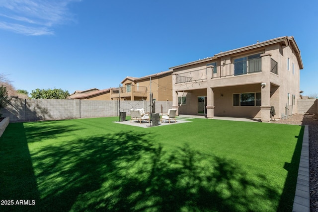 back of house featuring a yard, a patio, stucco siding, a balcony, and a fenced backyard