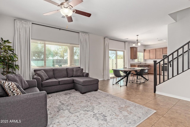 living area with light tile patterned floors, ceiling fan, stairway, and baseboards