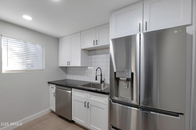 kitchen featuring tasteful backsplash, dark countertops, stainless steel appliances, white cabinetry, and a sink