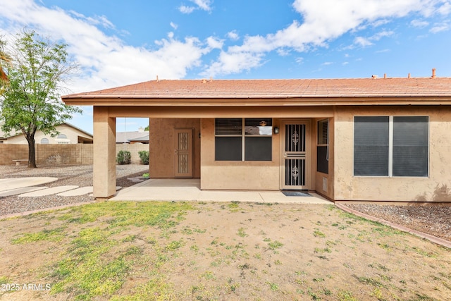 rear view of house with stucco siding, a patio area, and fence